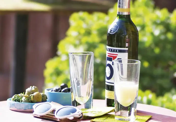 Ein Glas Pastis mit Anis Geschmack, Oliven und Sonnenbrille auf einem Tisch im Freien.
