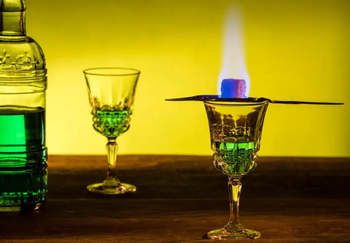 Grüner Absinth brennt über einem Zuckerwürfel in einem Glas. Die Zubereitung lässt die Absinth-Wirkung erahnen.