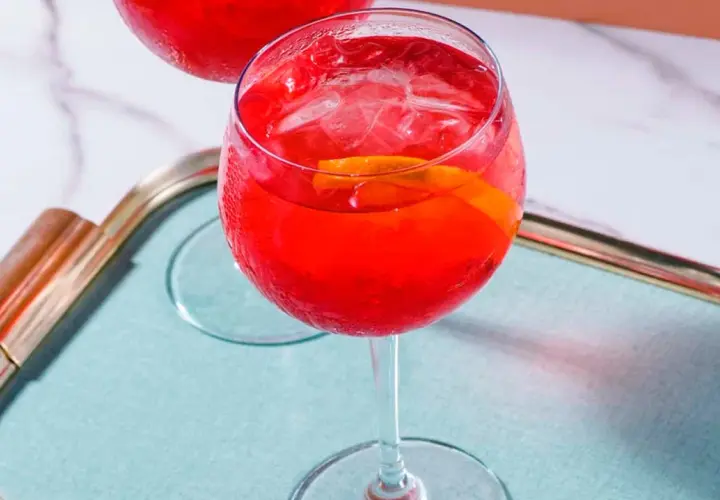 Erfrischender Campari Spritz mit Eis und Orangenscheibe auf einem Tablett.