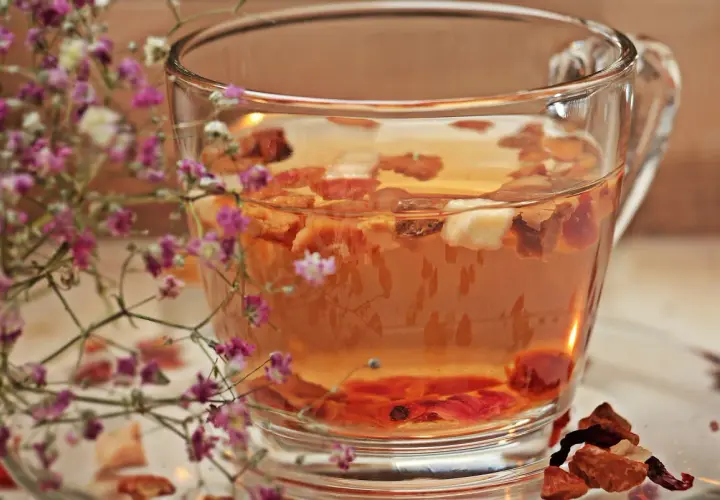 Ein Glas **Tee mit Schuss** und getrockneten Früchten, umrahmt von zarten rosa Blüten.