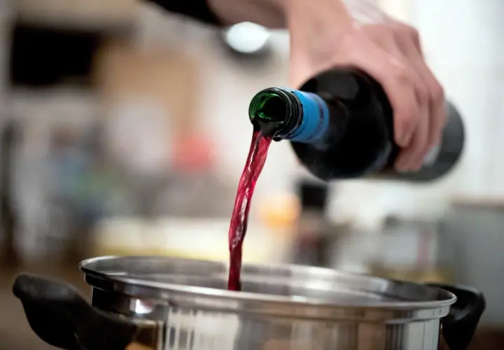 Roter Wein fließt aus einer Flasche in einen Topf. Perfekt als alkohol zum kochen für ein köstliches Gulasch.