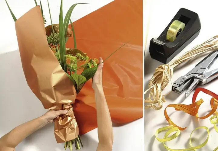 Anleitung: Blumen mit Packpapier verpacken. Hände arrangieren den Strauß, während orangefarbenes Papier bereitliegt. Werkzeuge wie Klebeband, Schere und Bänder sind daneben zu sehen.