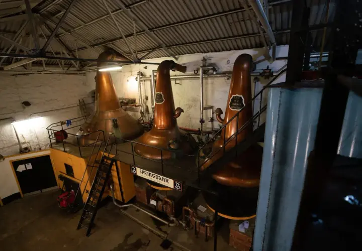 Drei große Kupfer-Brennblasen (pot still) in einer Brennerei, bereit zur Destillation.