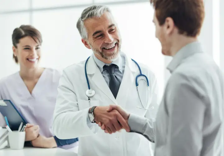Ein Arzt schüttelt einem Patienten die Hand, ein Lächeln der Zufriedenheit. Im Hintergrund eine lächelnde Krankenschwester. Ein schönes Bild für eine Danksagung Krankenhaus.