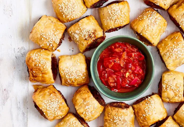 Goldbraune Würstchen im Blätterteig mit Sesam, daneben eine Schale mit roter Chutney-Sauce. Perfekt für schnelle Partysnacks zum Vorbereiten!