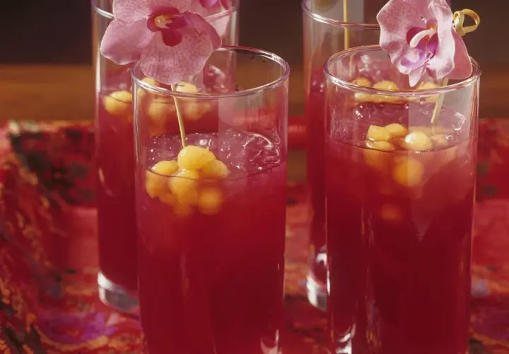 Erfrischende asiatische Cocktails mit Melonenbällchen und Orchideen auf einem roten, gemusterten Tuch.