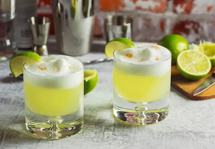 Zwei Pisco Sours mit Limettenspalten und Schaumkrone, bereit für den Genuss.