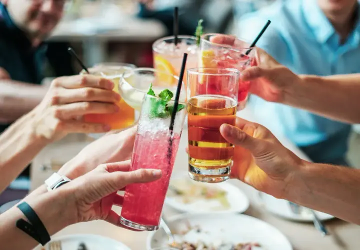 Hände heben bunte Cocktails zum Anstoßen. Eine ausgelassene Cocktailparty mit Freunden.