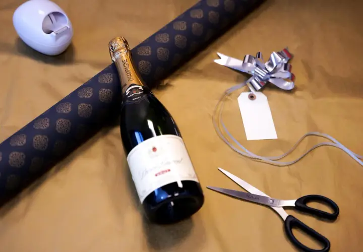 Vorbereitung, um mehrere Flaschen als Geschenk zu verpacken: Champagnerflasche, Geschenkpapier, Schere und Schleife liegen bereit.