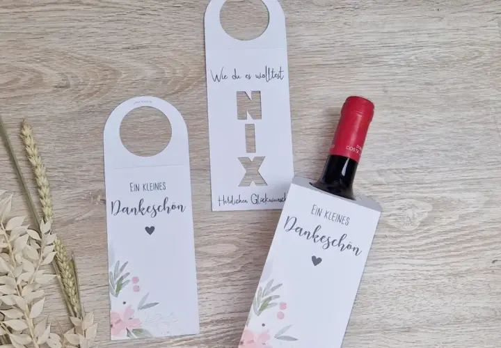 Eine Weinflasche mit Geld verpacken: weiße Hüllen mit floralem Muster und Schriftzug "Ein kleines Dankeschön".