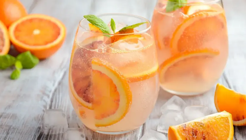 Erfrischender Aperol Lillet mit Blutorangenscheiben und Minze, serviert mit Eiswürfeln auf Holzhintergrund.