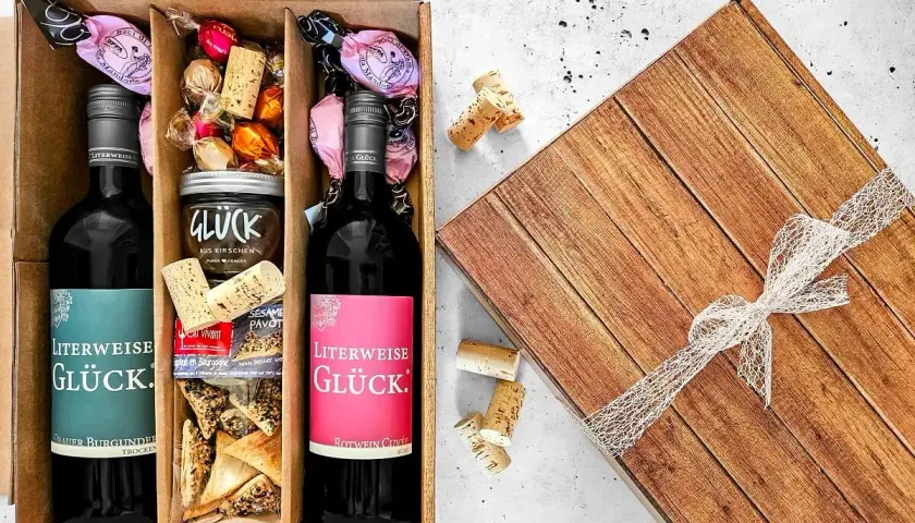 Ein liebevoll zusammengestellter Geschenkkorb zum selber machen: Zwei Flaschen Wein, Pralinen, Kirschmarmelade und Gebäck.