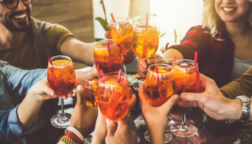 Freunde stoßen mit Aperol Spritz an. Eine bunte longdrinks liste für einen schönen Abend.