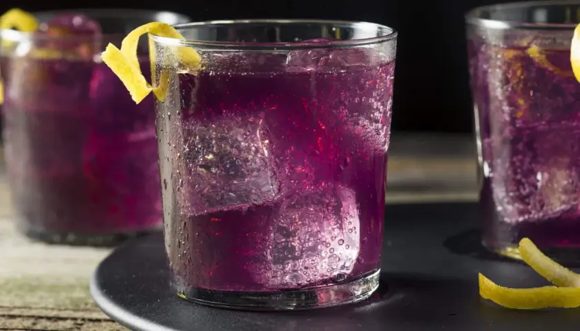 Erfrischender lila Cocktail mit Eis und Zitronenzeste.