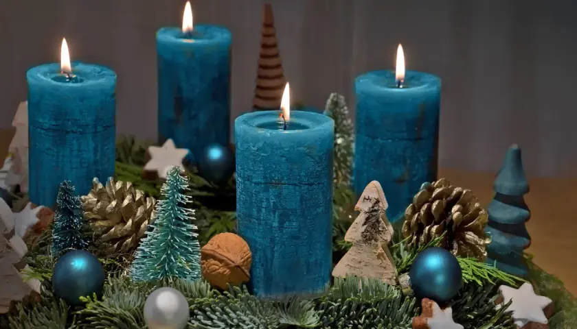 Ein selbstgebastelter Adventskranz mit vier blauen Kerzen, Tannenzweigen, Zapfen und kleinen Bäumchen.