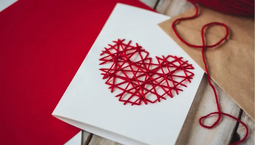 Eine selbstgemachte Valentinstagskarte mit einem roten Herz aus Garn. Perfekt zum Valentinstagskarte basteln.
