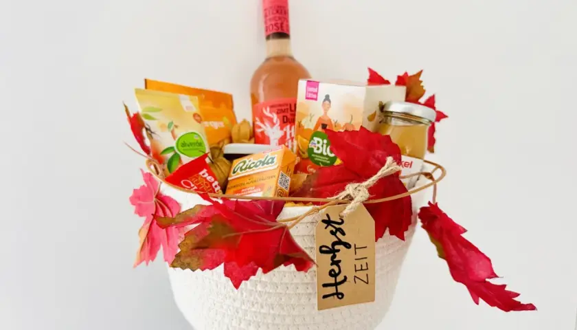 Ein liebevoll gefüllter Geschenkkorb zum Geburtstag, dekoriert mit Herbstlaub. Enthält Wein, Snacks und Honig.