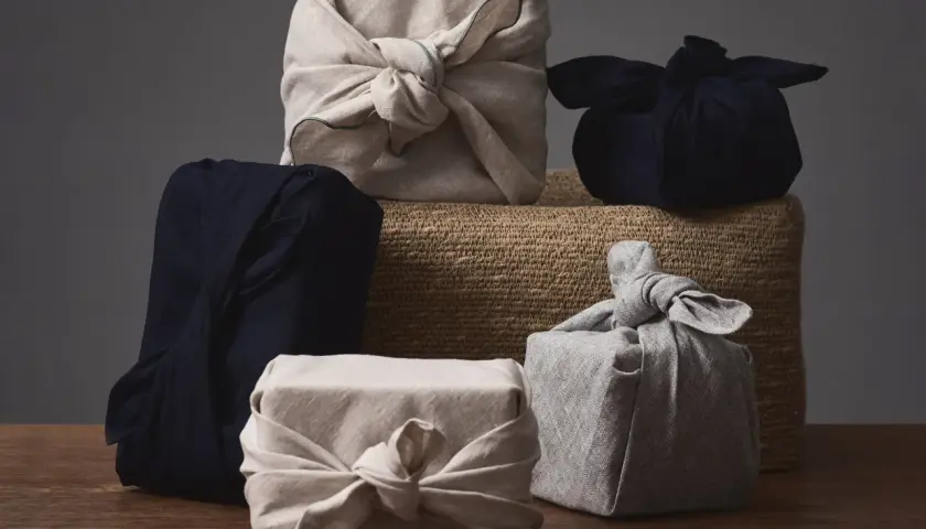 Fünf Geschenke, in Stoff gewickelt und mit Stoffschleifen verziert, warten darauf, ausgepackt zu werden. Eine stilvolle Art, Kleidung zu verpacken, als Geschenk.