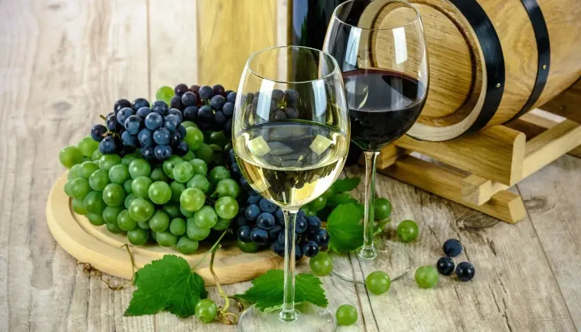 Zwei Gläser Wein, Trauben und ein Holzfass – perfekt für das Kochen mit Alkohol.