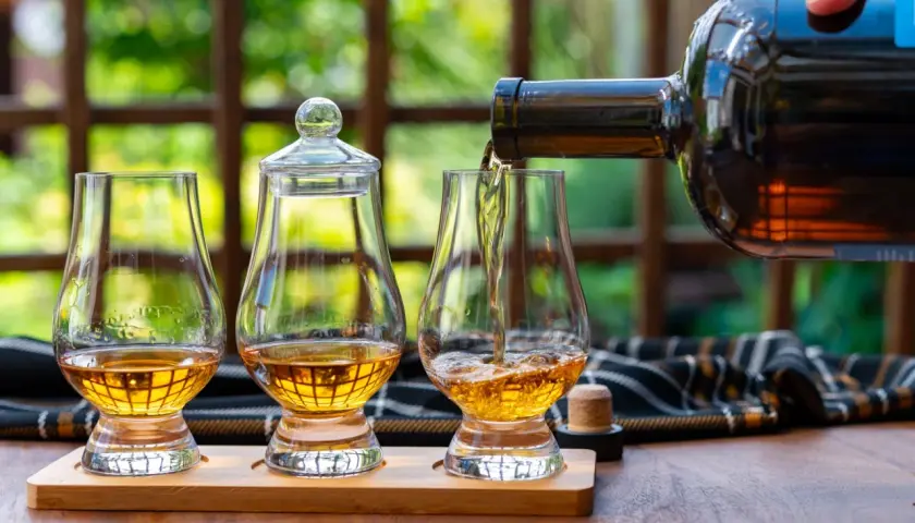 Ein Glas wird mit goldenem Whisky gefüllt, bereit, pur getrunken zu werden. Zwei weitere Gläser stehen daneben.