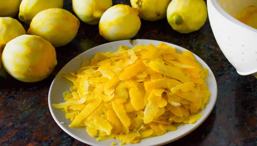 Zitronenschalen liegen auf einem Teller, bereit, um Limoncello herzustellen. Mehrere ganze Zitronen sind im Hintergrund zu sehen.