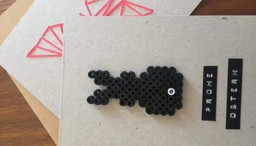 Selbstgemachte Osterkarte: Ein schwarzer Osterhase aus Perlen und ein rotes Muster auf Karton. Frohe Ostern!