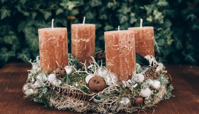 Natürlicher Adventskranz Idee mit vier braunen Kerzen, Moos, Federn und kleinen Glaskugeln auf einem Holztisch.