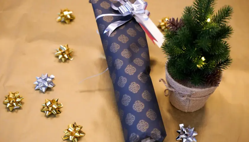 Eine **Flasche weihnachtlich verpacken** ist einfach mit diesem dunklen Geschenkpapier und silberner Schleife. Kleine Schleifen und ein Mini-Tannenbaum schmücken die Szene.