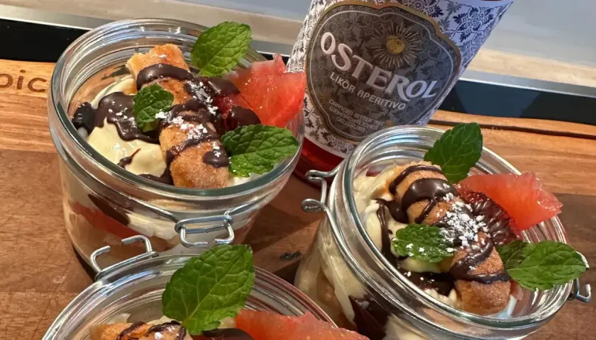 Italienischer Schnaps nach dem Essen: Leckere Desserts im Glas mit Schokolade, Früchten und Minze, daneben eine Flasche Osterol Likör.