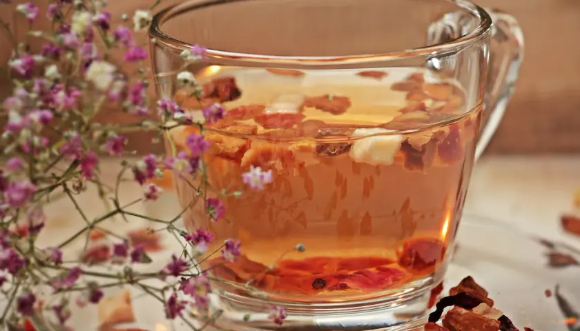 Ein Glas **Tee mit Schuss** und getrockneten Früchten, umrahmt von zarten rosa Blüten.