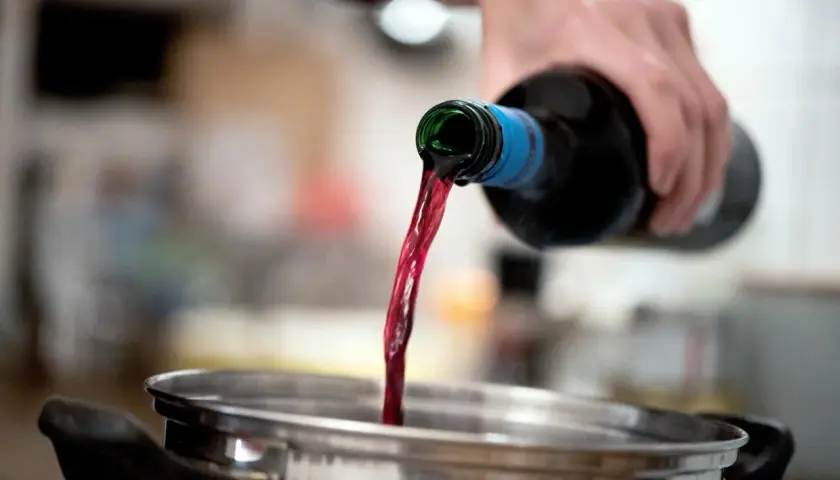 Roter Wein fließt aus einer Flasche in einen Topf. Perfekt als alkohol zum kochen für ein köstliches Gulasch.