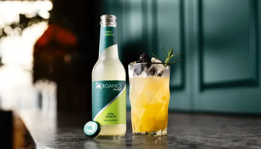 Erfrischender bitter lemon cocktail mit Brombeere und Rosmarin. Daneben eine Flasche "The Organics by Red Bull Bitter Lemon".