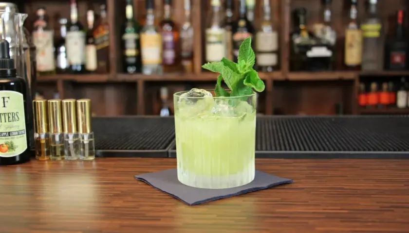 Ein erfrischender grüner Cocktail mit Minze, Eis und einer Flasche Bitters. Perfekt, um zu sehen, mit was man Tequila mischt.