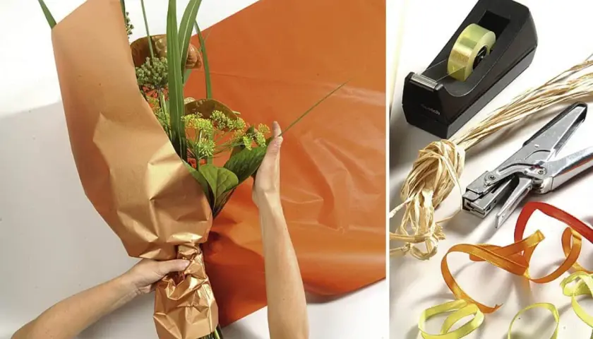 Anleitung: Blumen mit Packpapier verpacken. Hände arrangieren den Strauß, während orangefarbenes Papier bereitliegt. Werkzeuge wie Klebeband, Schere und Bänder sind daneben zu sehen.