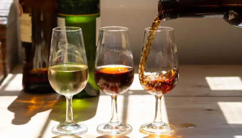 Drei Gläser mit Sherry Aperitif, eines hell, eines dunkelrot, das dritte wird gerade gefüllt.