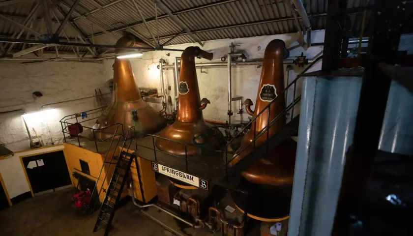 Drei große Kupfer-Brennblasen (pot still) in einer Brennerei, bereit zur Destillation.