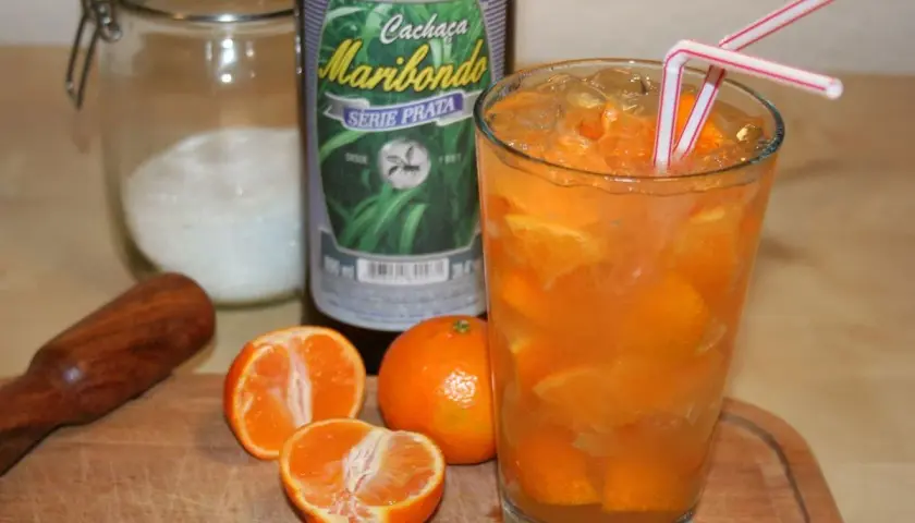 Ein Glas mit Eis und Orangenscheiben, daneben eine Flasche "Cachaça Maribondo". So wird Cachaça, ein brasilianischer Zuckerrohrschnaps, oft serviert.