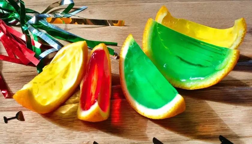 Farbige Jelly Shots in Orangenschalen, dekoriert mit Party-Konfetti. Ein süßer Genuss für jede Feier!