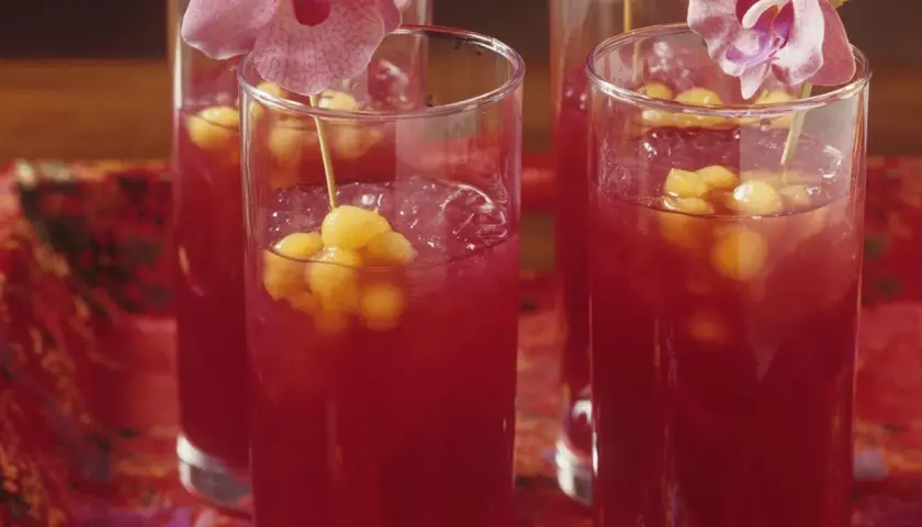 Erfrischende asiatische Cocktails mit Melonenbällchen und Orchideen auf einem roten, gemusterten Tuch.