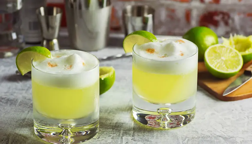 Zwei Pisco Sours mit Limettenspalten und Schaumkrone, bereit für den Genuss.