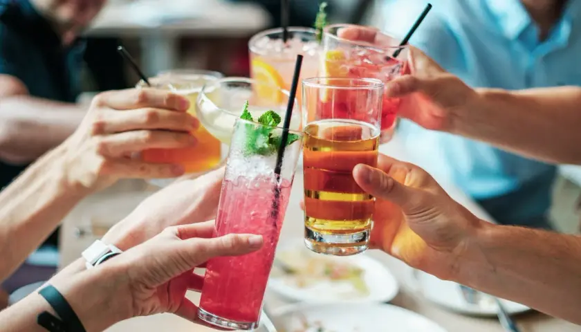 Hände heben bunte Cocktails zum Anstoßen. Eine ausgelassene Cocktailparty mit Freunden.