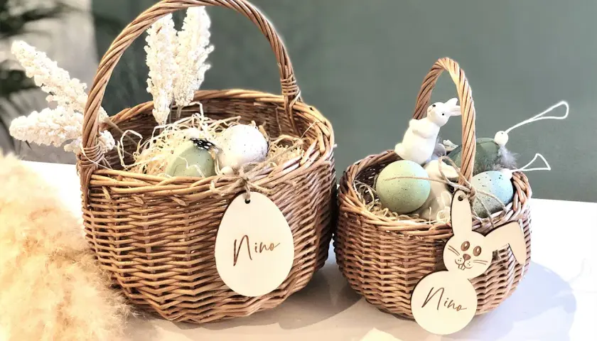 Zwei geflochtene Körbe mit Osterdeko: Eier, Federn, weiße Blumen und Holzanhänger mit Namen. Tolle Osterkorb Ideen für Kinder.