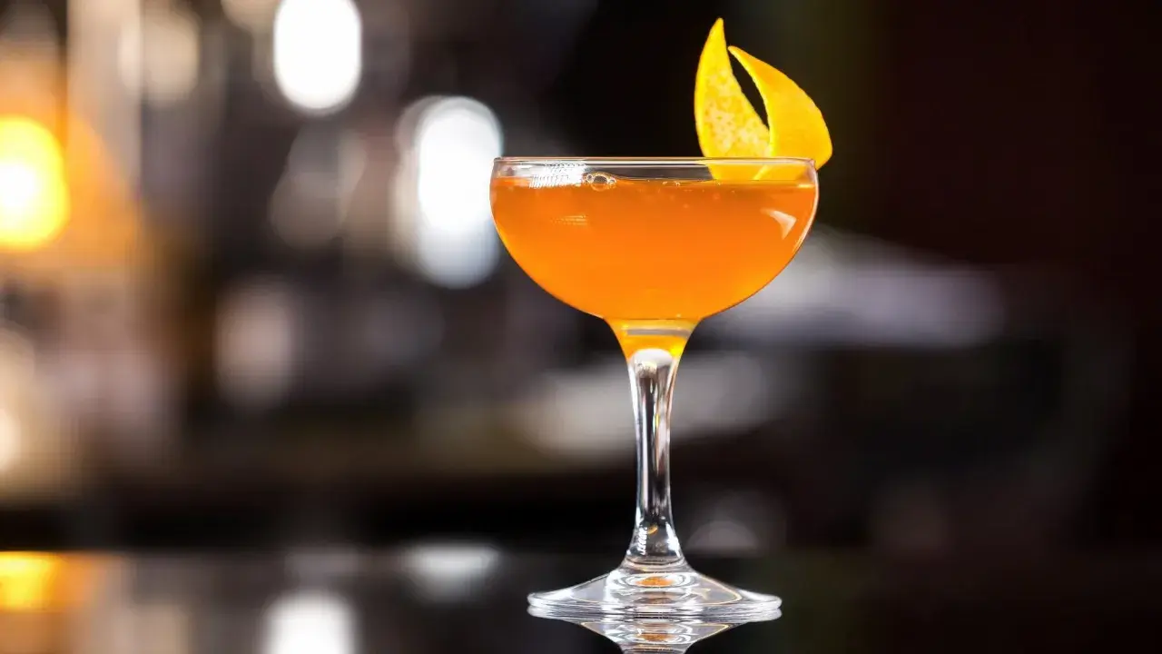 Ein leuchtend oranger Martini Rosso Cocktail, garniert mit einer Orangenzeste, steht auf einer dunklen Oberfläche.