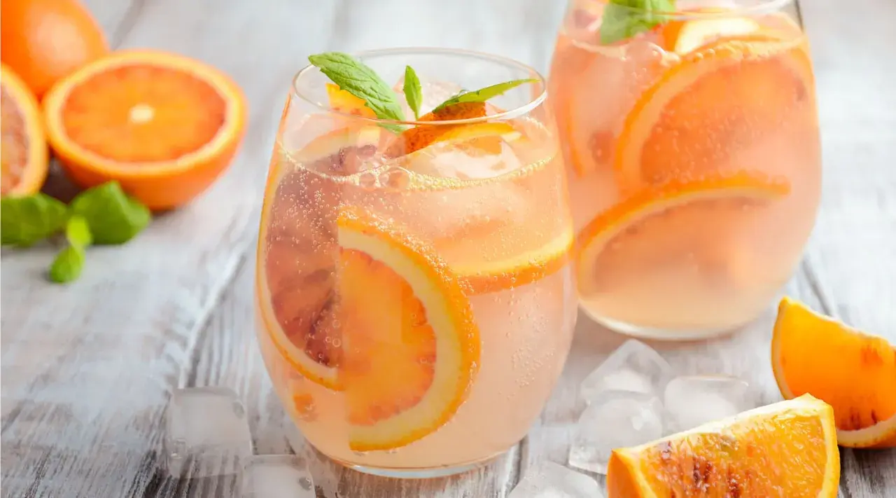 Erfrischender Aperol Lillet mit Blutorangenscheiben und Minze, serviert mit Eiswürfeln auf Holzhintergrund.