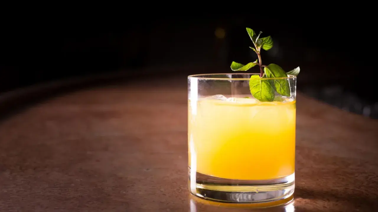 Ein erfrischender Galliano Cocktail mit Eis und Minze auf einem Holztresen.