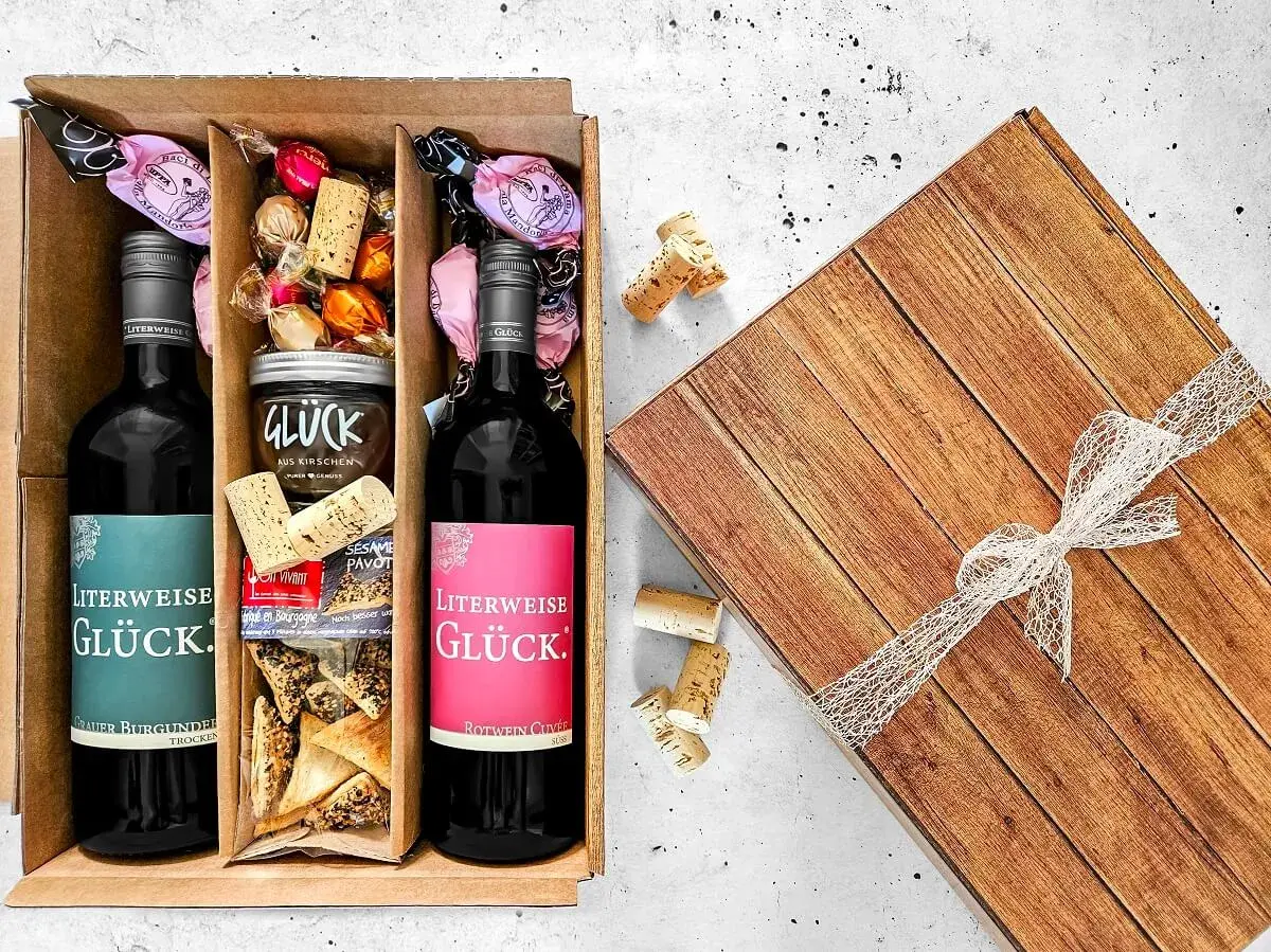 Ein liebevoll zusammengestellter Geschenkkorb zum selber machen: Zwei Flaschen Wein, Pralinen, Kirschmarmelade und Gebäck.