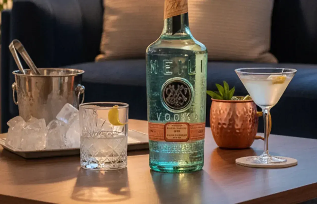 Flasche MEILI VODKA neben Eiswürfeln und Cocktails. Woraus wird Wodka hergestellt? Aus Getreide oder Kartoffeln, destilliert und gefiltert.