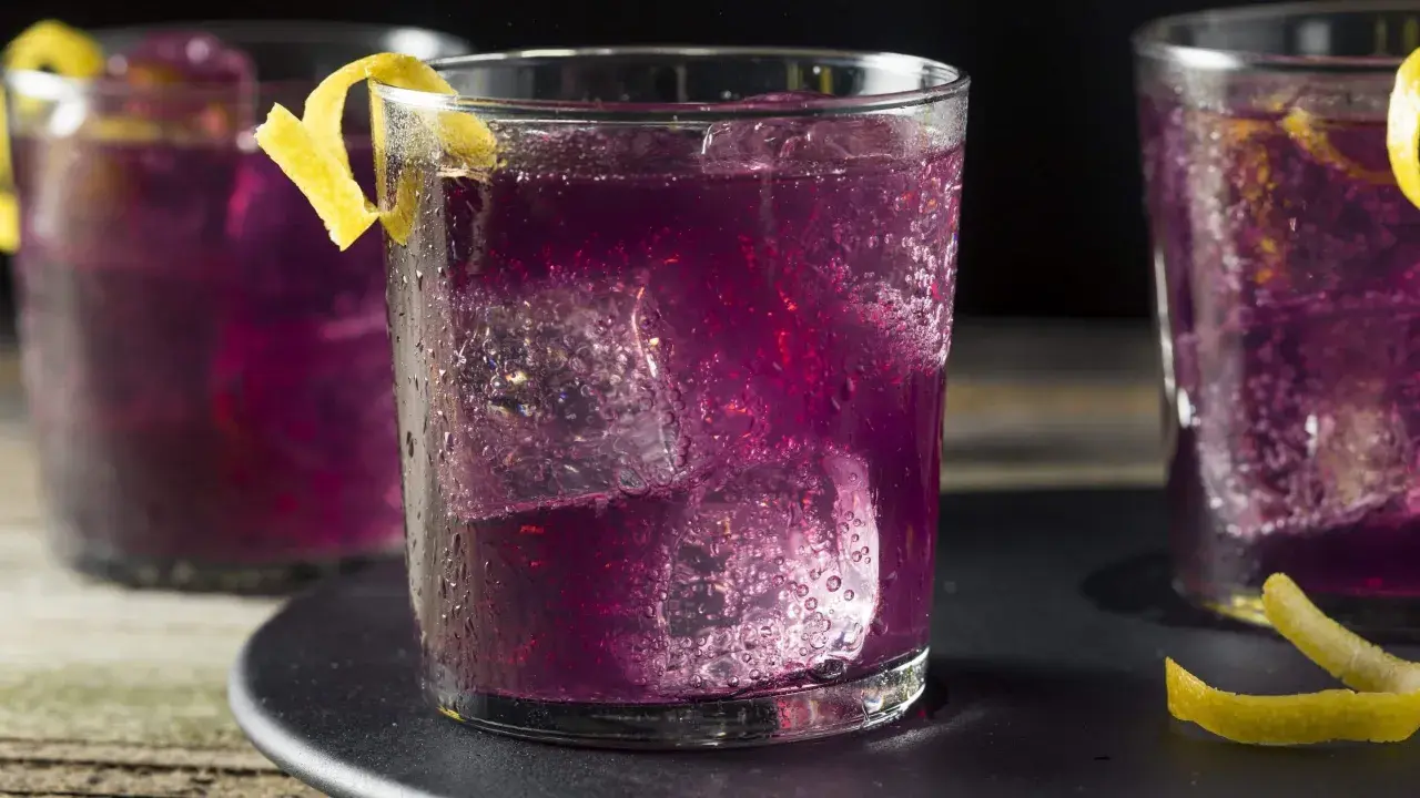 Erfrischender lila Cocktail mit Eis und Zitronenzeste.