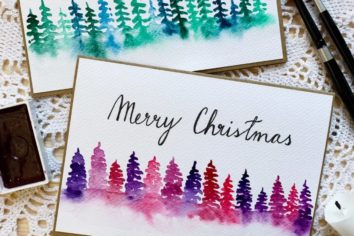 Zwei handgemalte Weihnachtskarten mit Aquarell-Tannenbäumen in Lila- und Grüntönen. Perfekt zum Thema Weihnachtskarten selber malen.