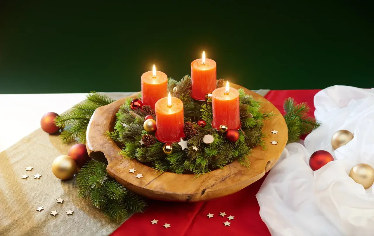 Ein selbstgemachter Adventskranz auf einem Holzteller mit vier brennenden Kerzen, Tannenzweigen, Kugeln und Sternen.